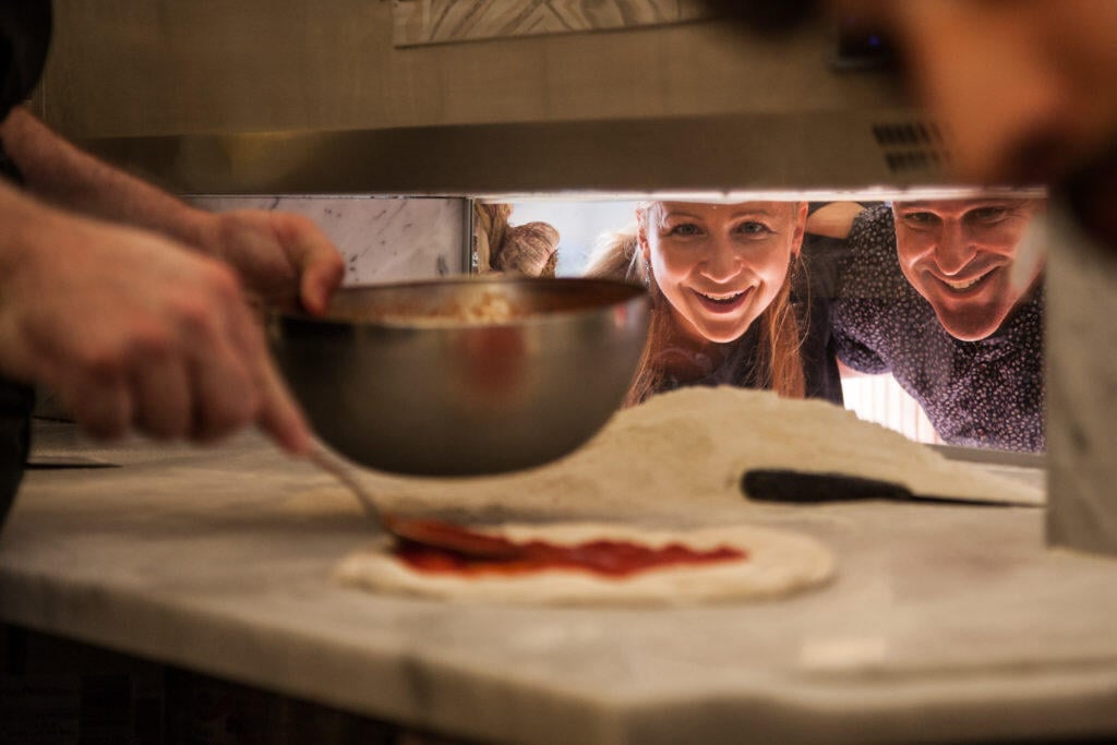 Two people watching pizza being made